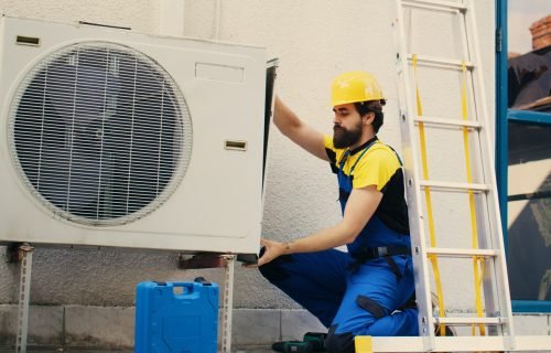 Professional worker starting work on malfunctioning air conditioner, using power drill to take apart condenser side coil panel. Capable electrician dismantling hvac system to check for faulty wires